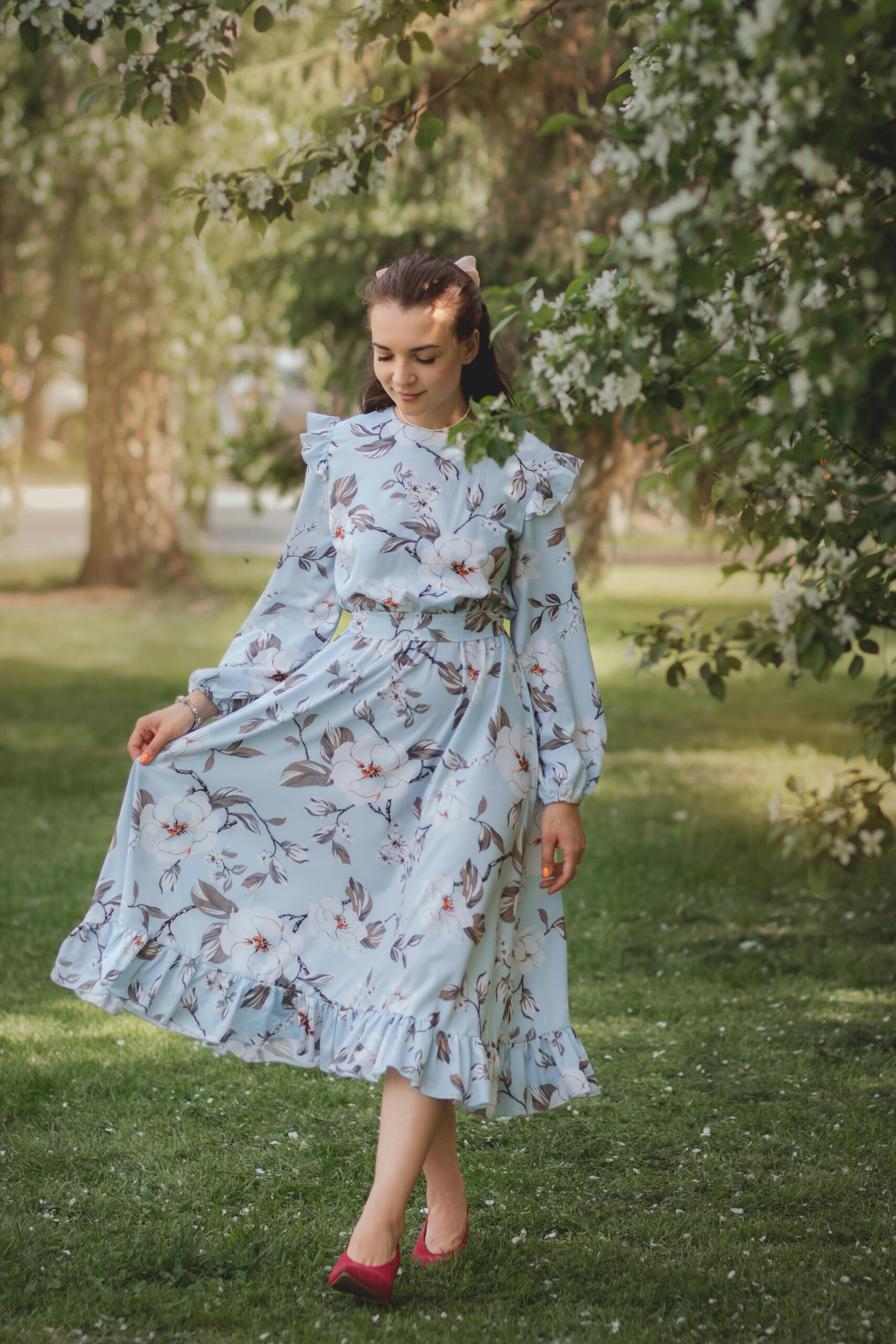 Woman in a flowing floral dress walking gracefully in a lush green park setting.